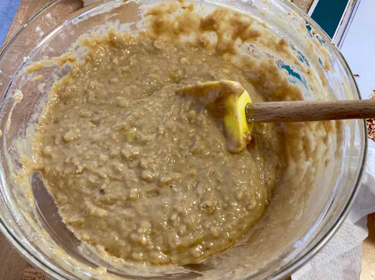 Mixing banana bread batter in glass bowl with spatula.