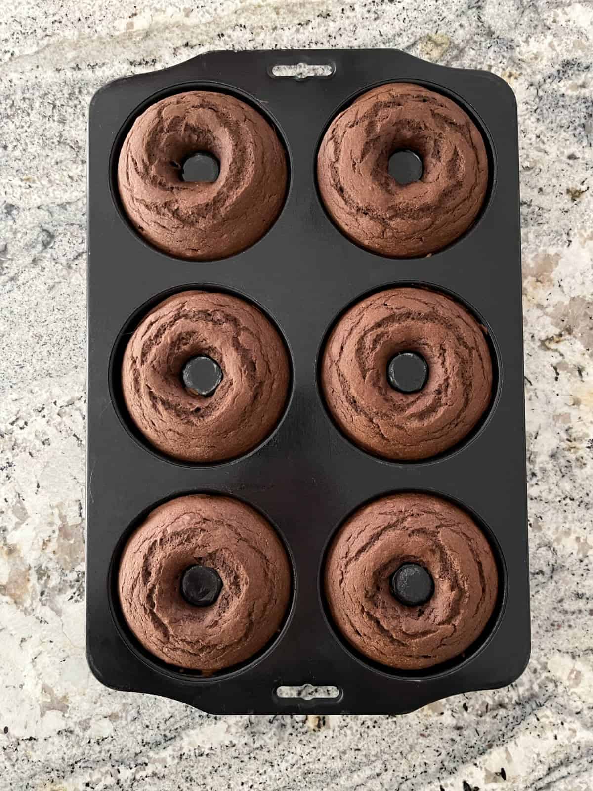 Baked mint chocolate donuts in pan on granite counter.