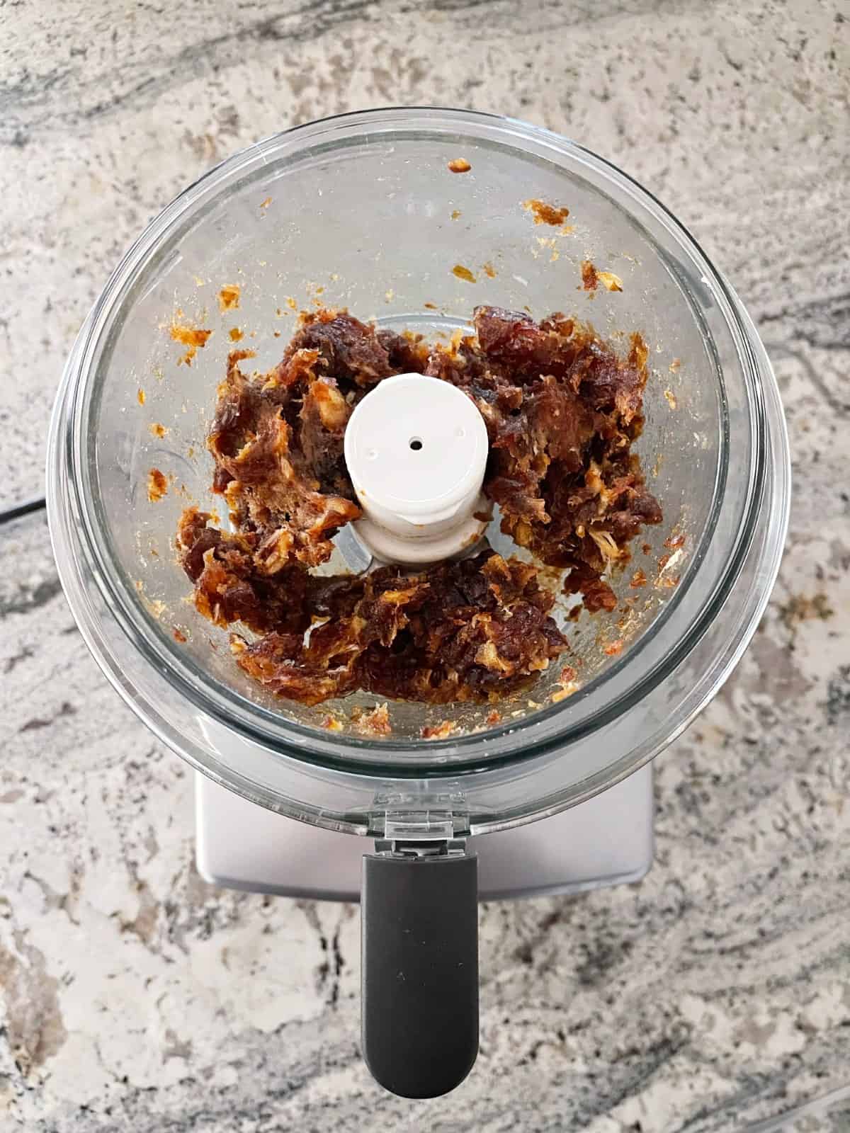 Finely chopped dates in food processor on granite counter.