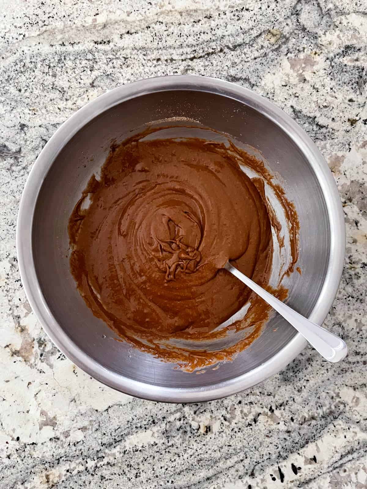 Devil's food cake mix combined with pumpkin puree in stainless mixing bowl on granite.