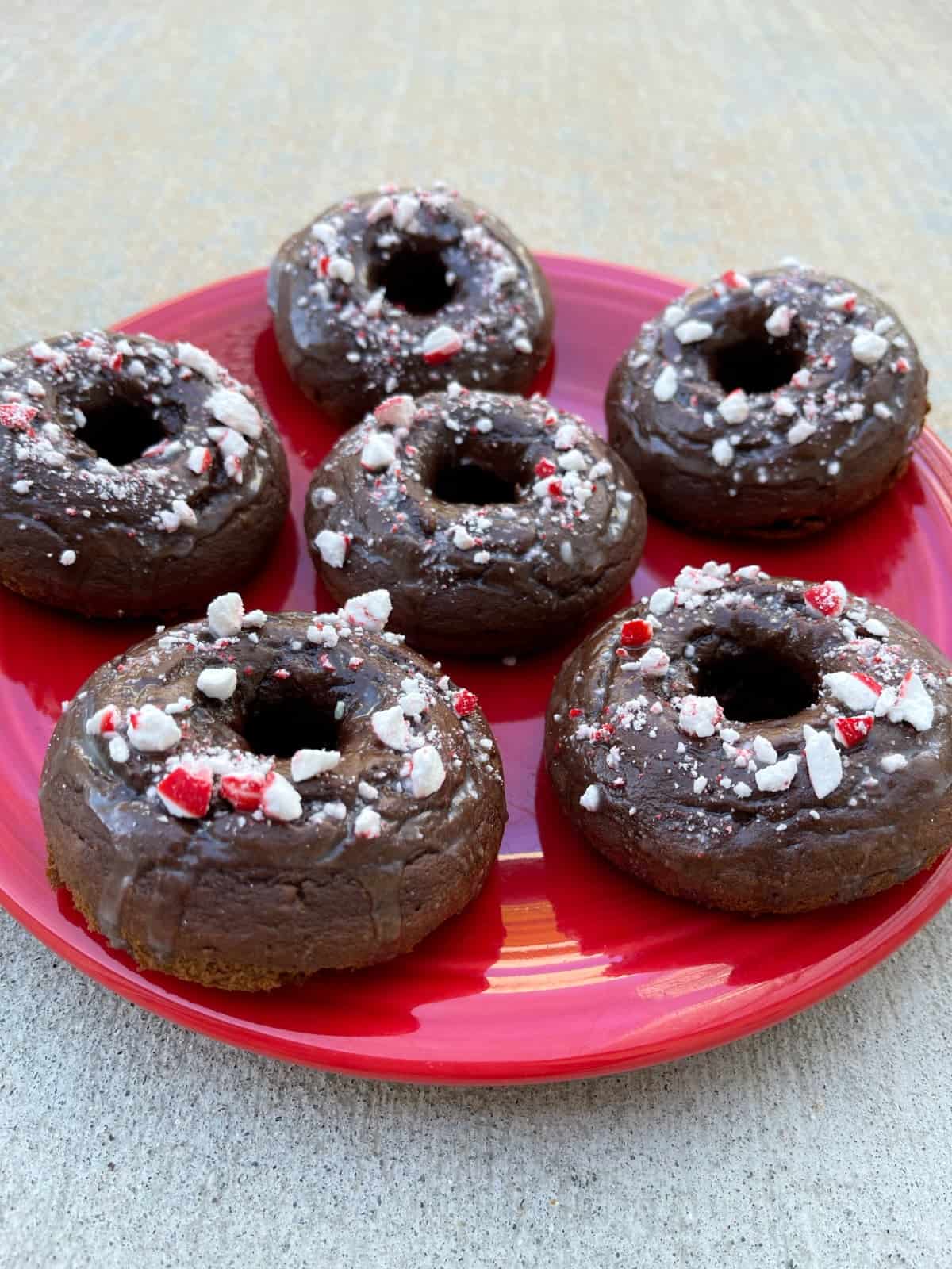 Mint chocolate glazed donuts topped with crushed candy canes on red plate.