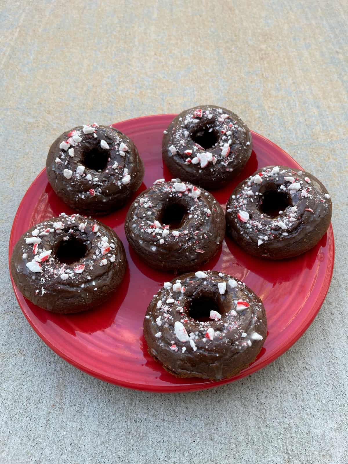 Crushed candy cane topped mint chocolate glazed donuts on red plate.