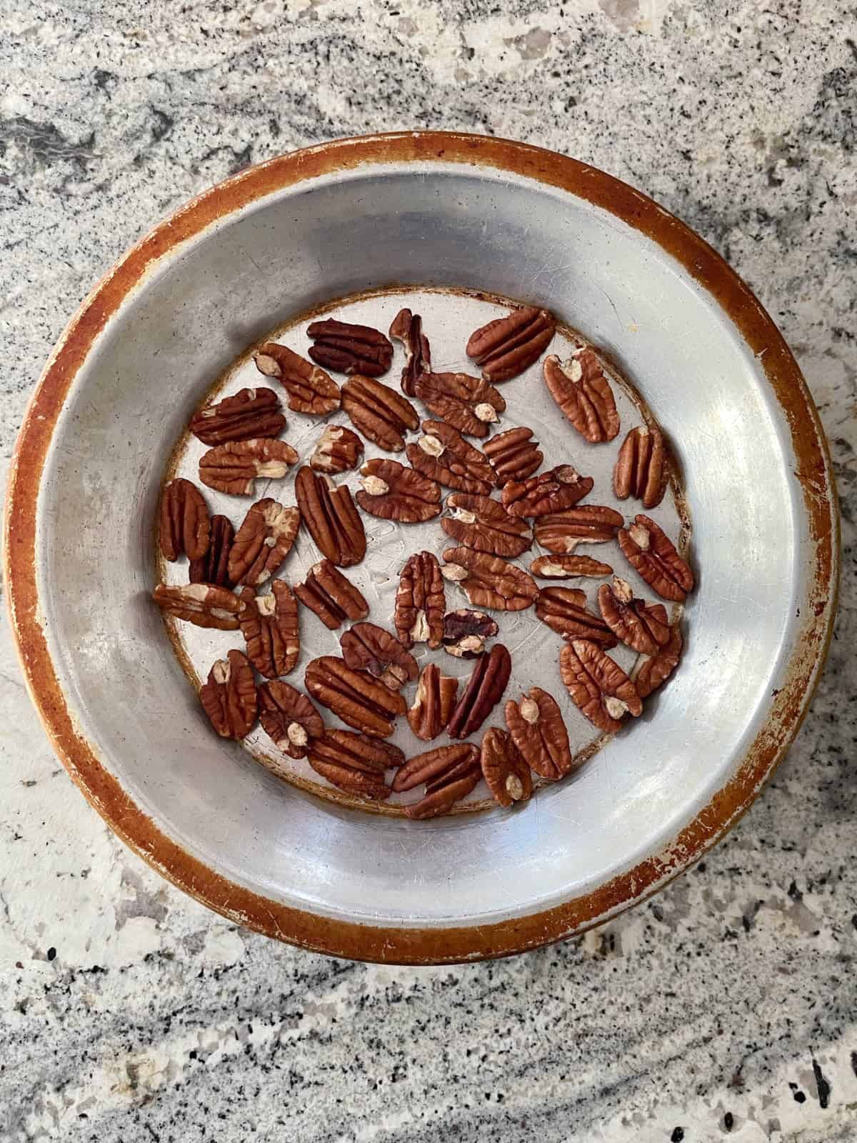 Toasted whole pecans in pie tin on granite counter.