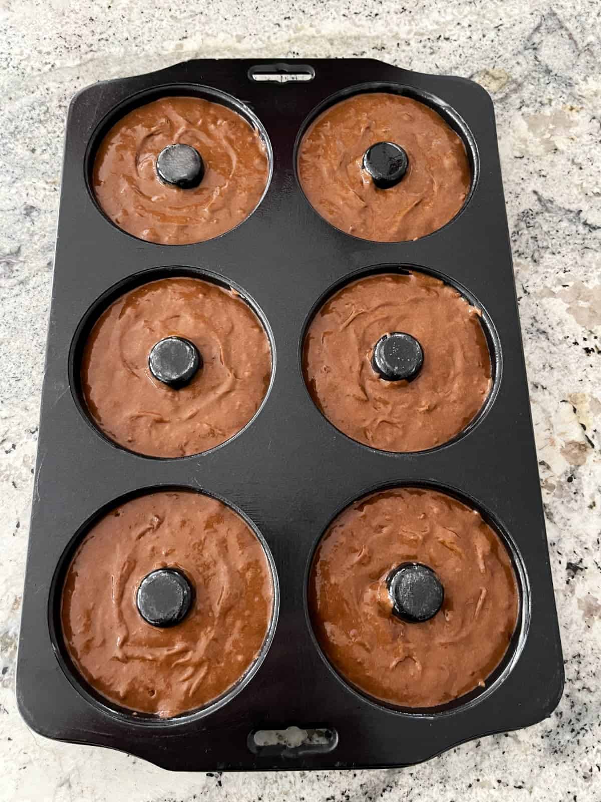 Unbaked mint chocolate donuts in baking pan.