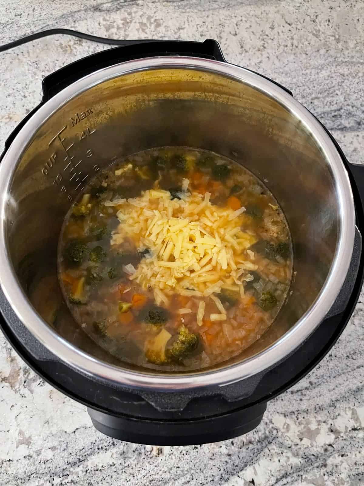 Adding shredded cheddar to broccoli cheese soup in Instant Pot.