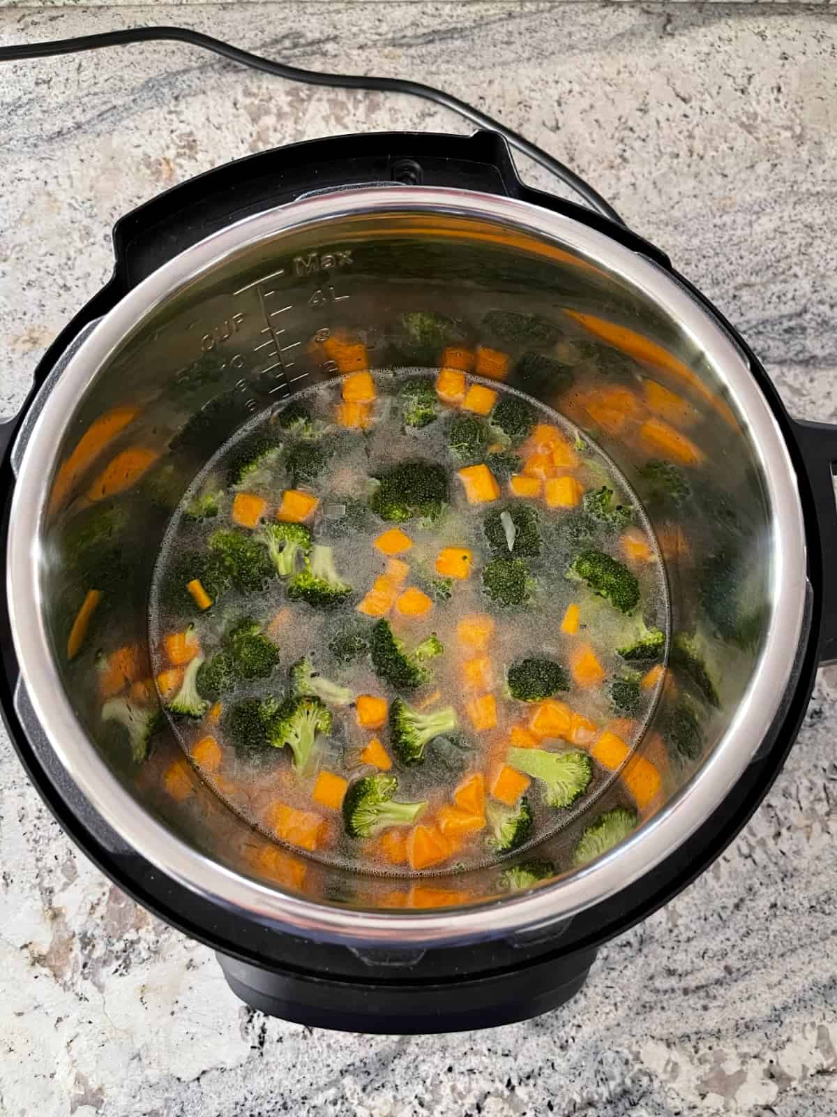 Instant Pot with broth, broccoli florets and cubed butternut squash on granite counter.