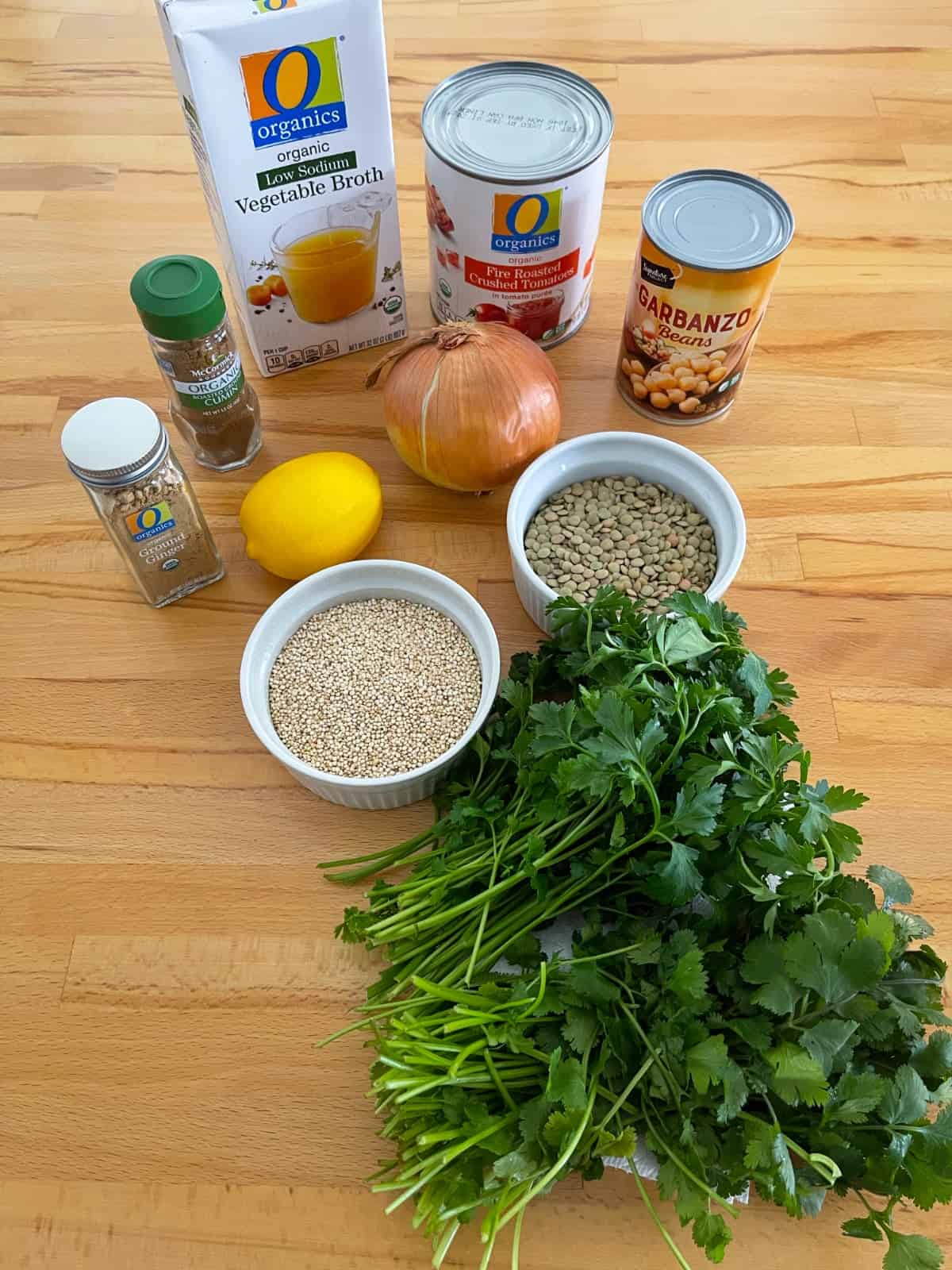Ingredients for making soup including vegetable broth, canned tomatoes, garbanzo beans, dried lentils, quinoa, lemon, onion, cilantro and parsley.