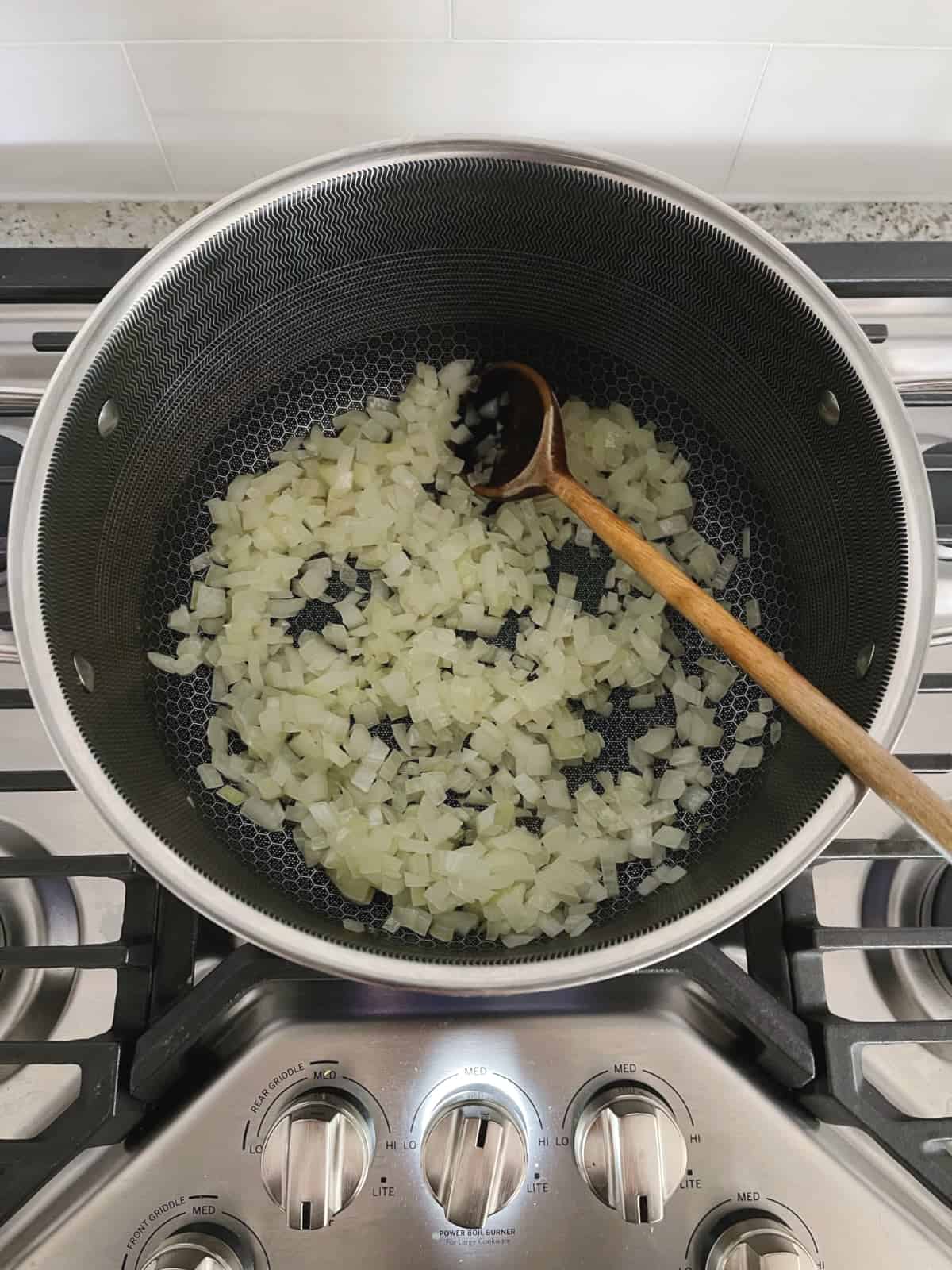 Cooking chopped onions in large sauce pan and stirring with wooden spoon.