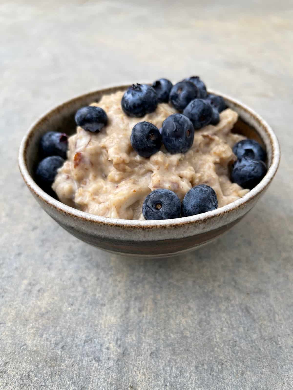 Slow cooker almond date oatmeal topped with fresh blueberries in ceramic bowl.