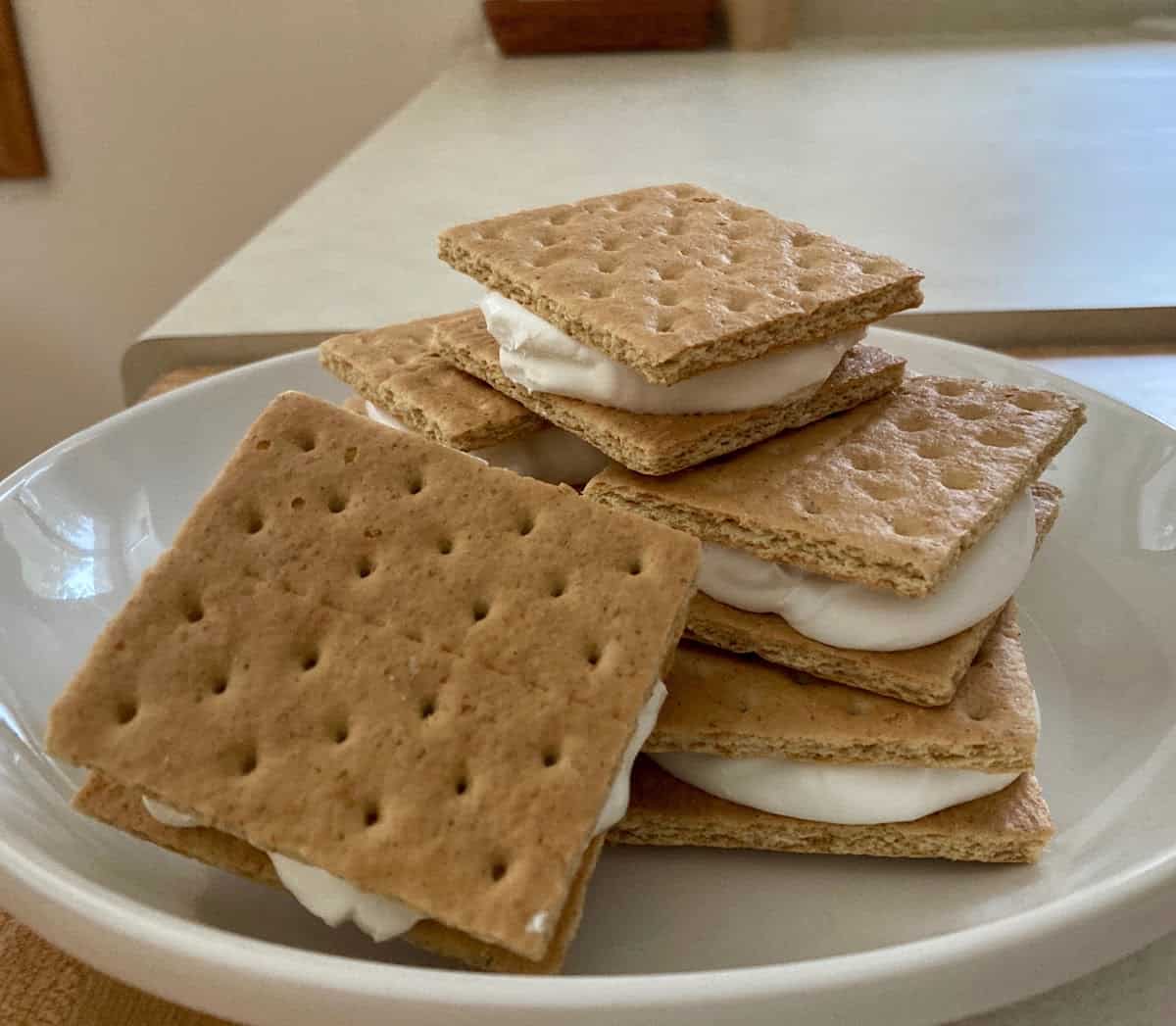 Frozen graham cracker cook whip sandwiches stacked on a white plate.