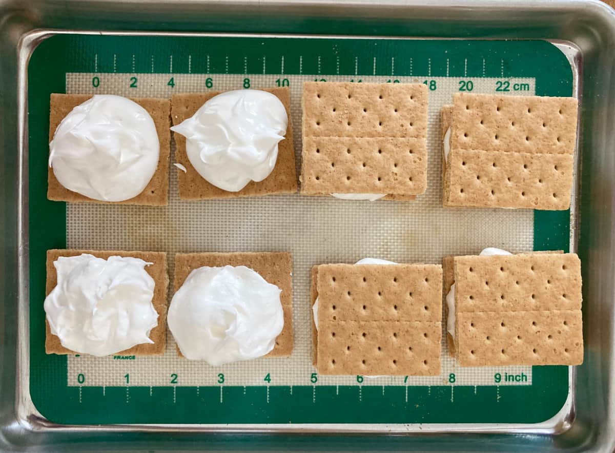 Assembling graham cracker cool whip sandwiches on cookie sheet.