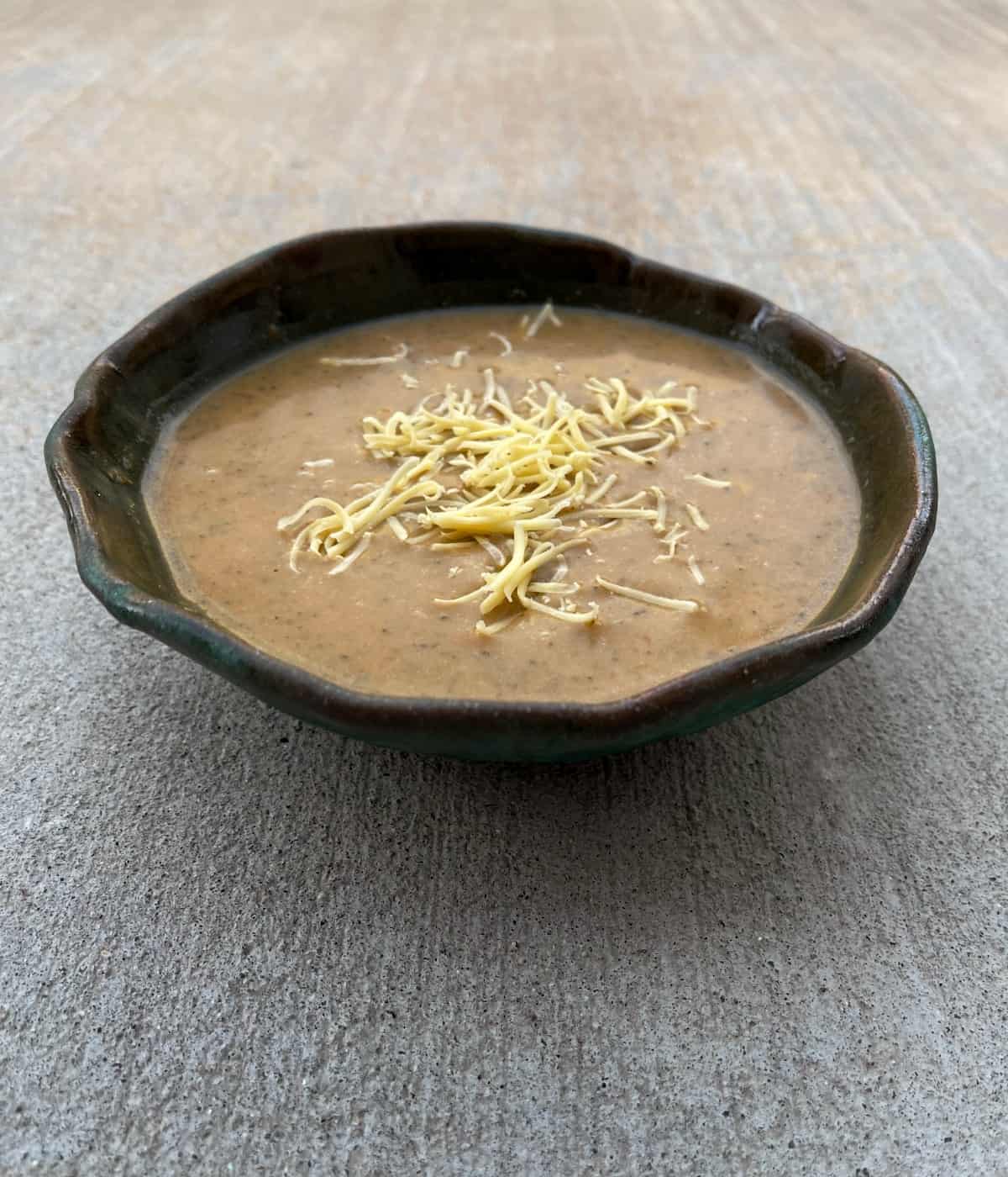 Broccoli cheese soup on pottery bowl topped with shredded cheddar.