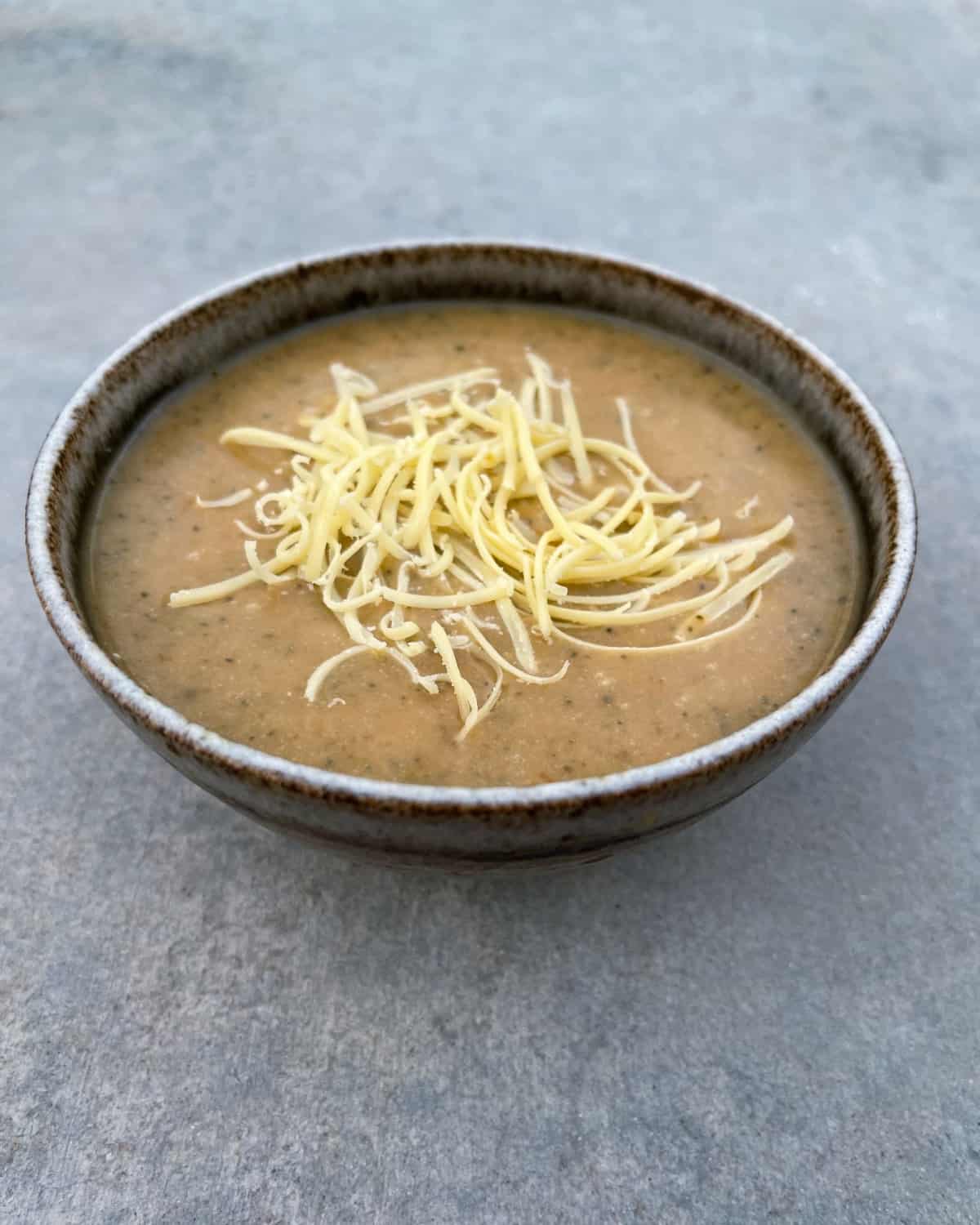 Instant pot broccoli cheddar soup in ceramic bowl topped with shredded cheese.