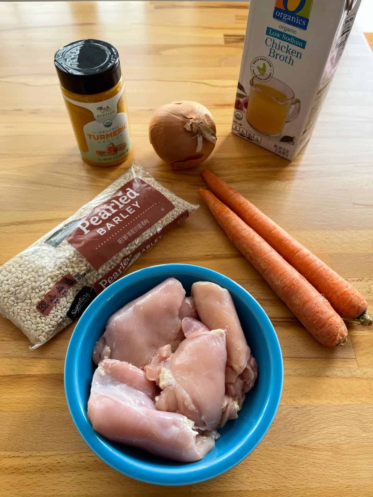 Stew ingredients including ground turmeric, onion, carrots, barley, chicken thighs and chicken broth.