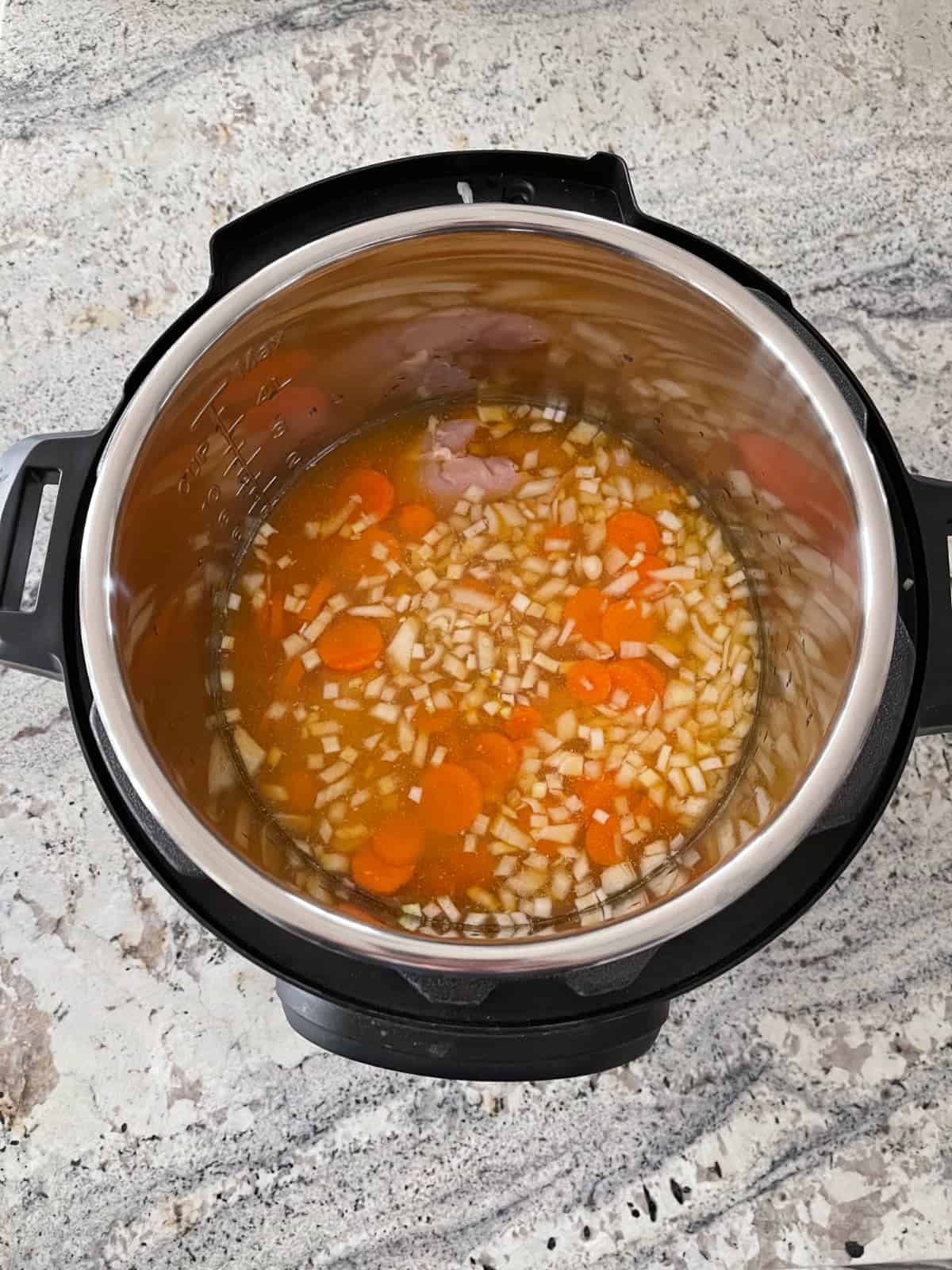 Uncooked chicken barley stew with onions and carrots in instant pot.