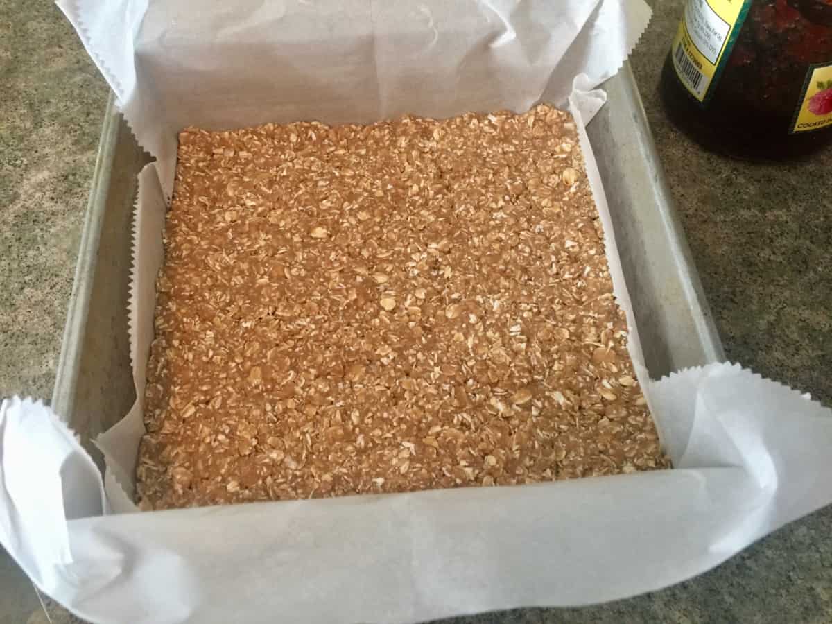 Parchment lined baking pan with unbaked oat crust patted into the bottom.