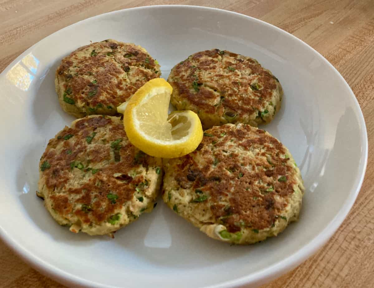 Four tuna patties on a white serving plate with fresh lemon.