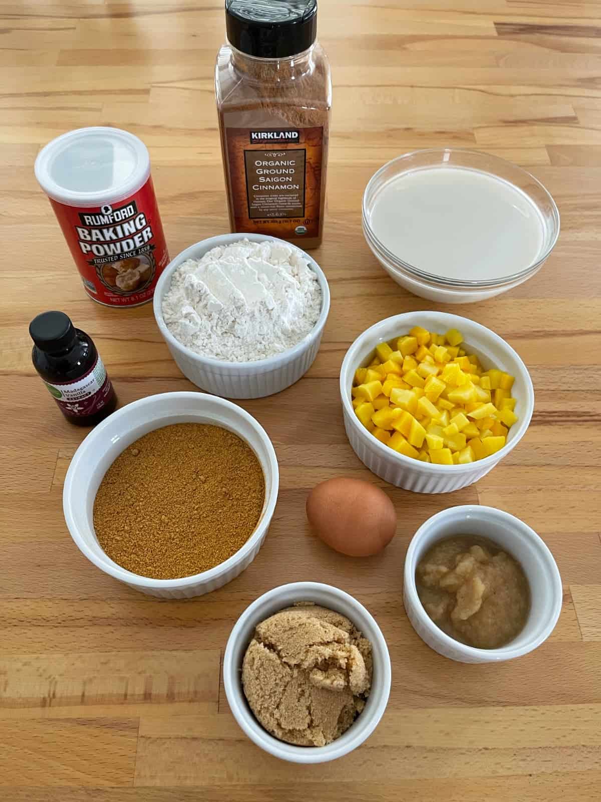 Ingredients for making muffins, including baking powder, cinnamon, flour, almond milk, diced mango, applesauce, egg, crushed FiberOne cereal, Truvia brown sugar blend.