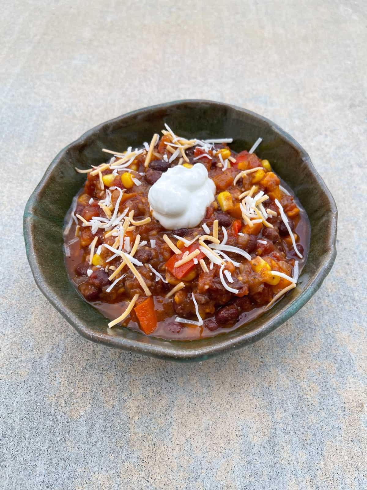 Black bean sweet potato chili topped with shredded cheese and dollop of lite sour cream in green pottery bowl.