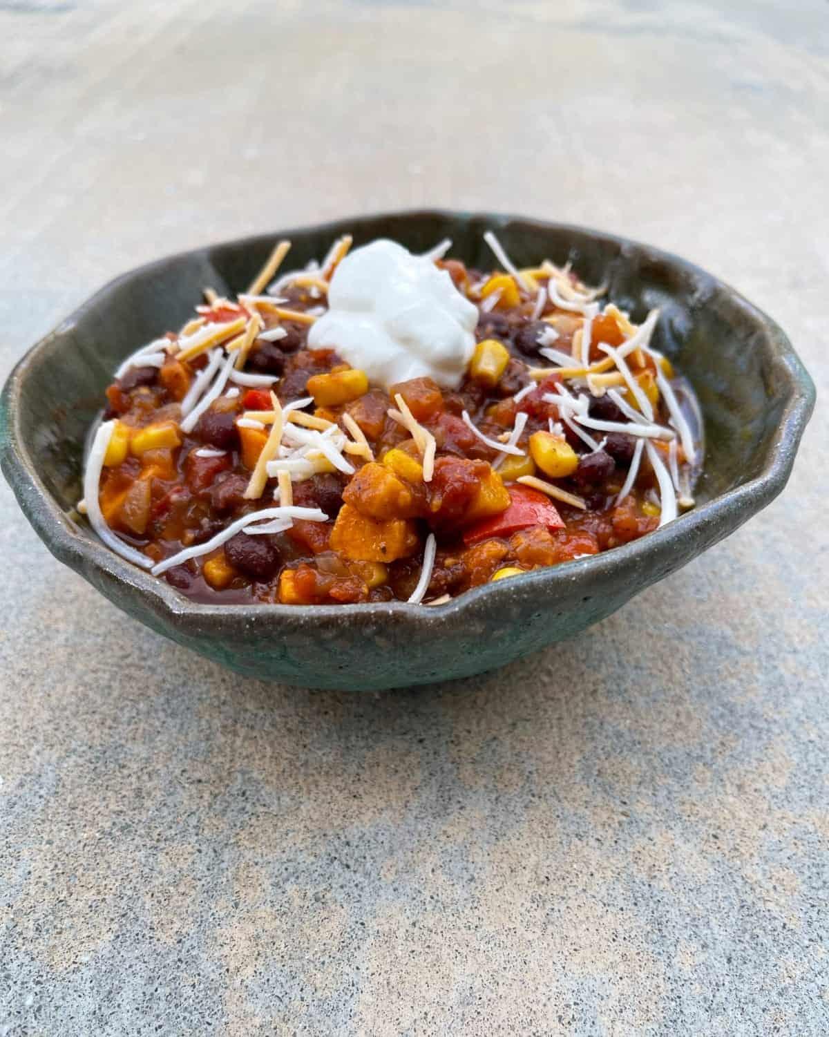 Bowl of instant pot black bean sweet potato vegetarian chili sprinkled with shredded cheese.