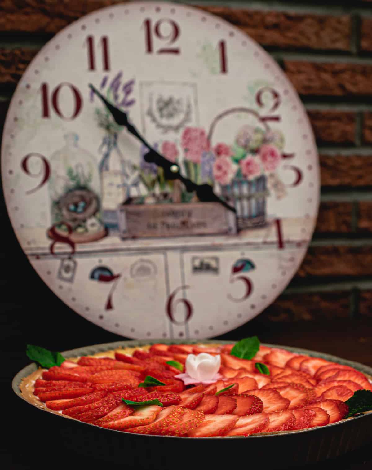 Old-fashioned decorative wall clock in background near plate of sliced strawberries.