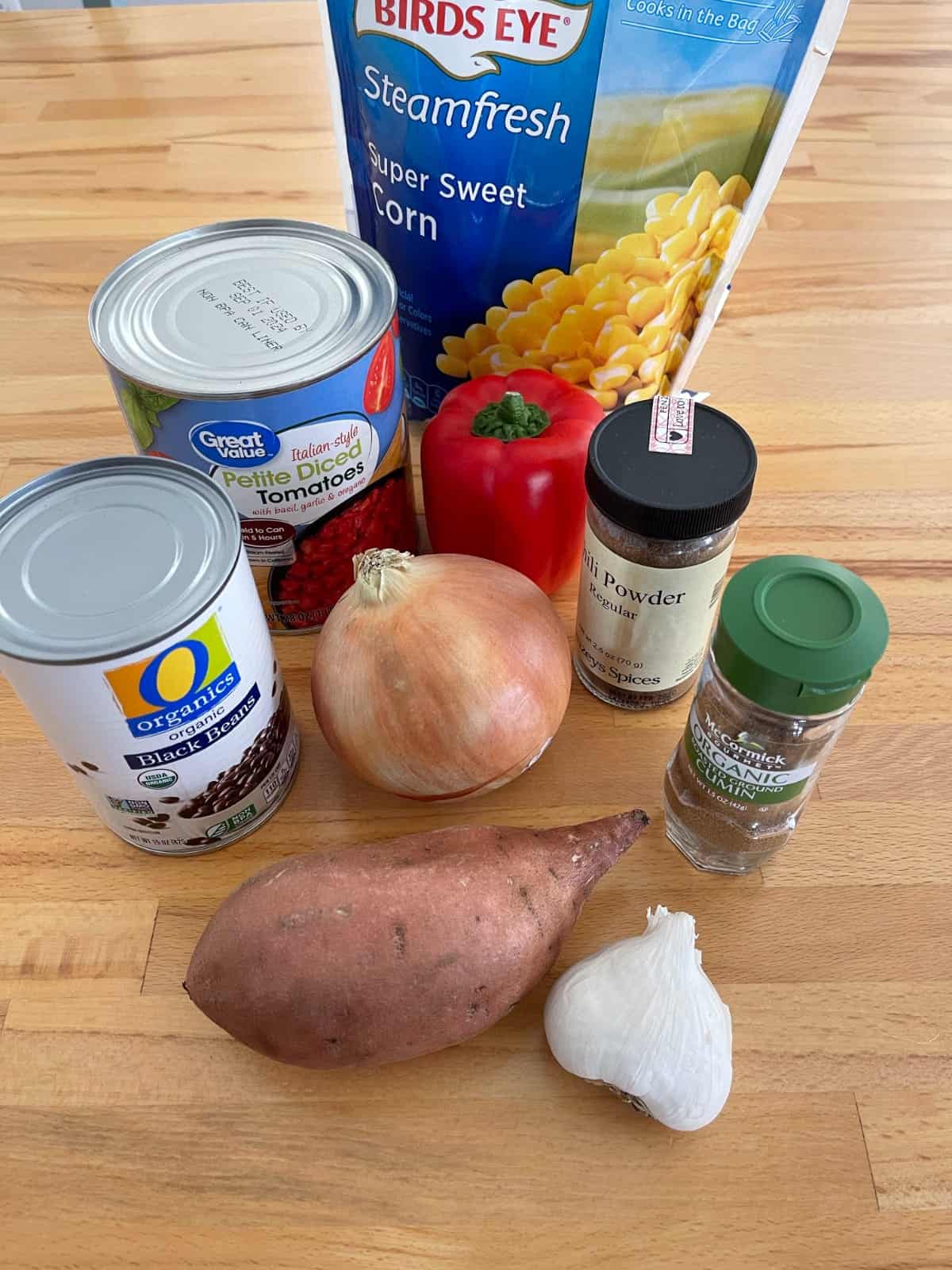 Ingredients for making chili, including sweet potato, onion, garlic, corn, black beans, diced tomatoes, bell pepper and chili powder.