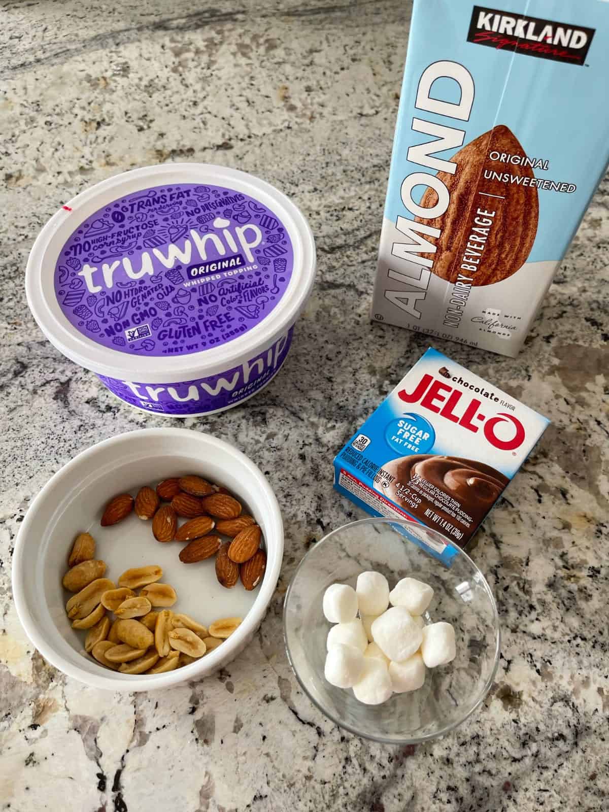 Ingredients for making rocky road pudding parfaits including almond milk, Truwhip, mini marshmallows, nuts and sugar-free instant chocolate jello pudding mix.