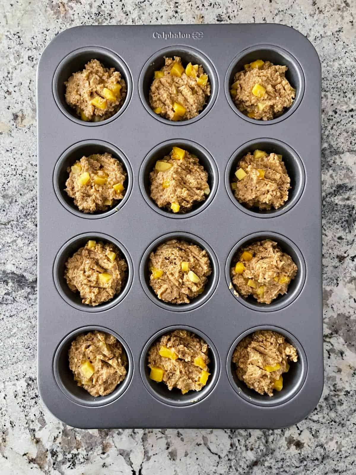 Unbaked mango muffins in muffin pan.
