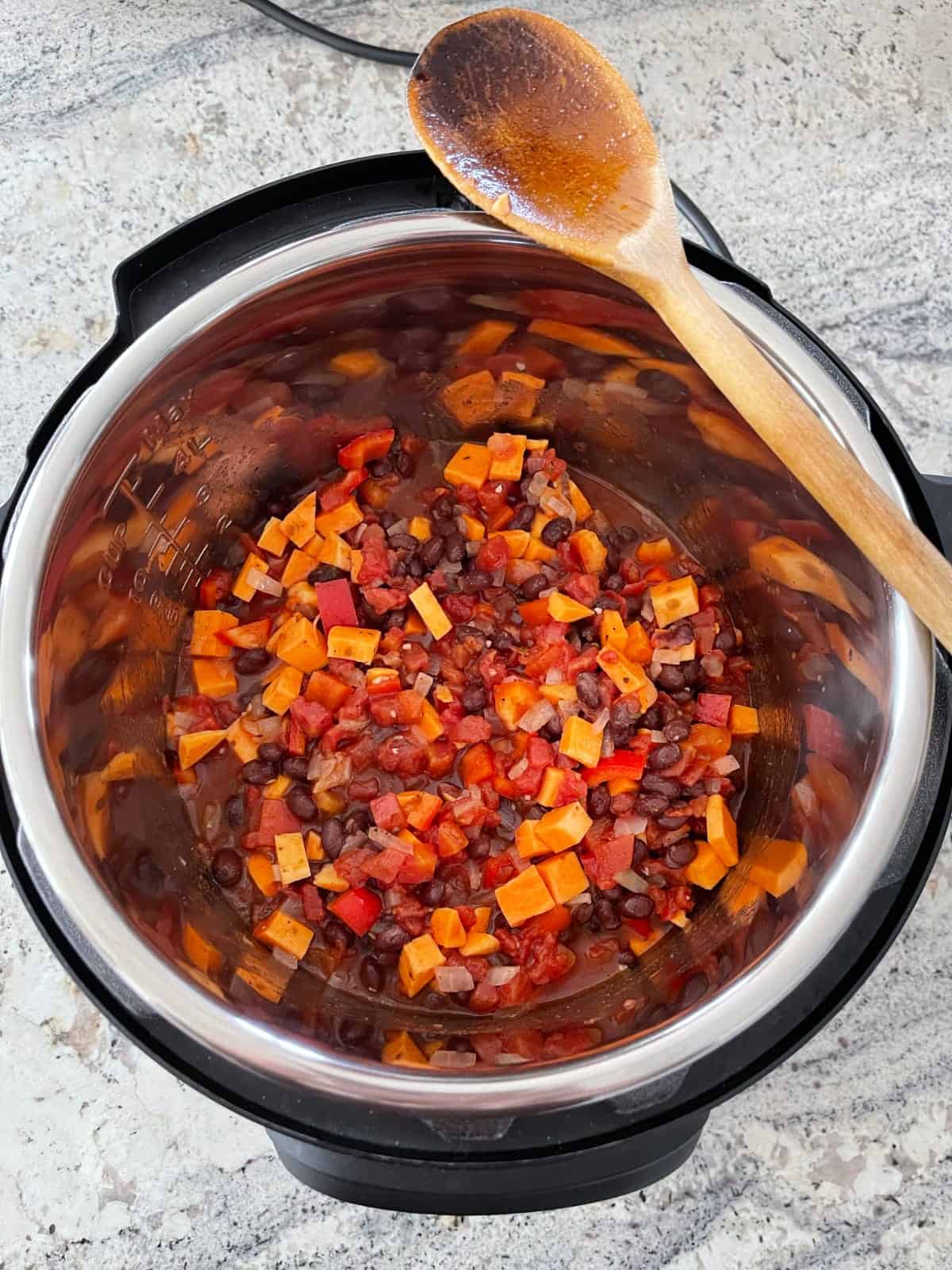 Uncooked black bean sweet potato chili in Instant Pot with wooden spoon.