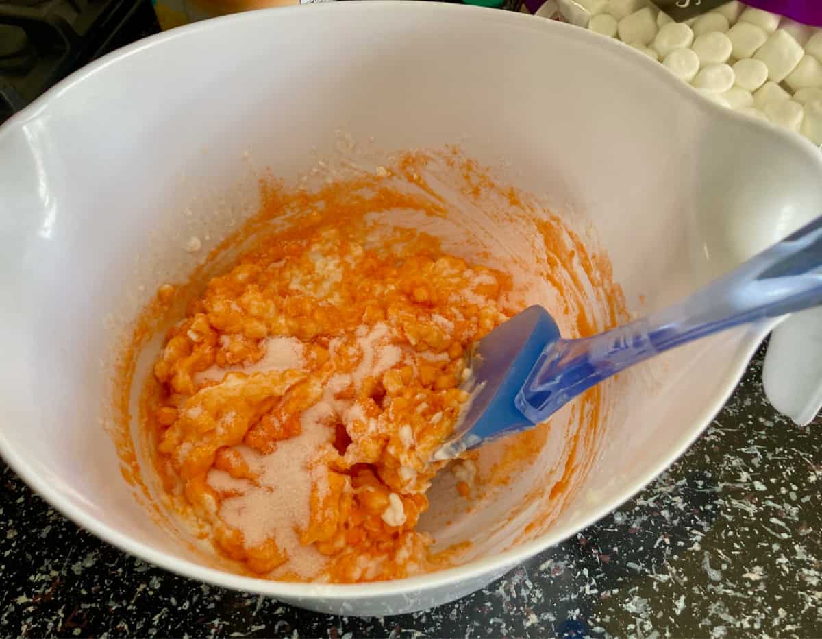 Mixing orange jello with cottage cheese in white bowl.