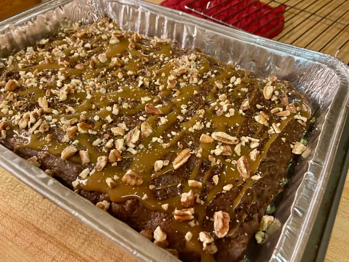 Fresh baked chocolate turtle cake topped with caramel sauce and chopped pecans in foil pan.