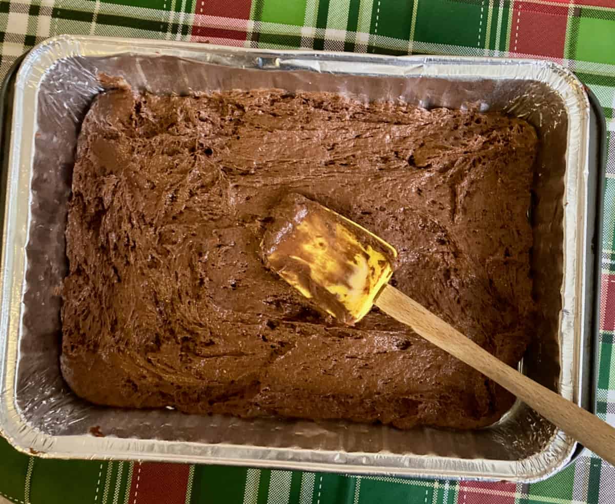 Spreading chocolate cake batter into foil pan with spatula.