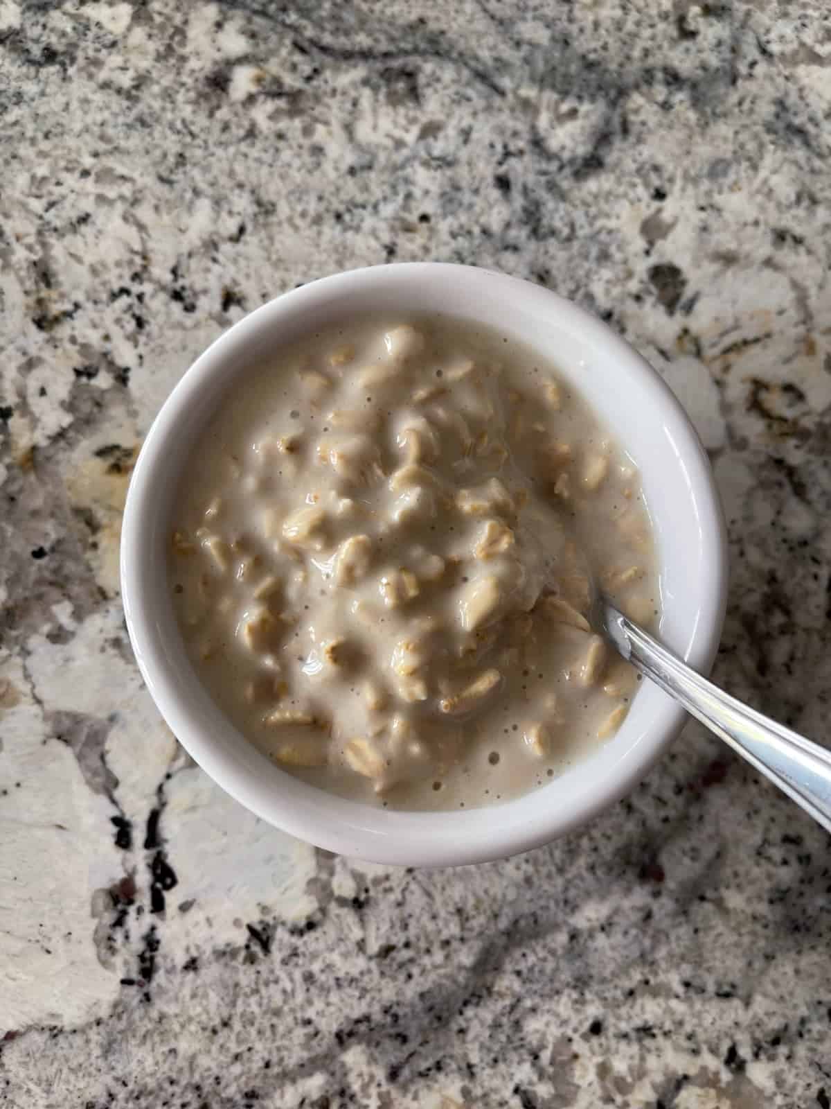 Cheesecake overnight oats without berries in small white bowl with spoon.