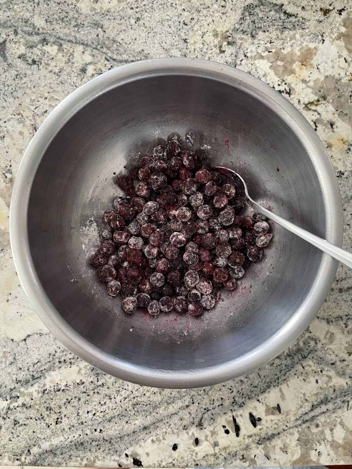 Tossing frozen blueberries in flour in mixing bowl.