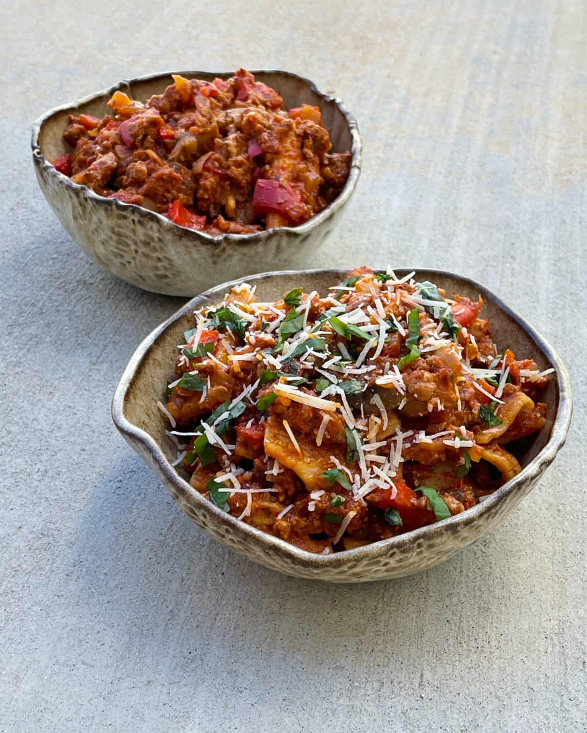 Instant Pot Rigatoni pasta and meat sauce in two bowls, one plane and one topped with basil and Parmesan