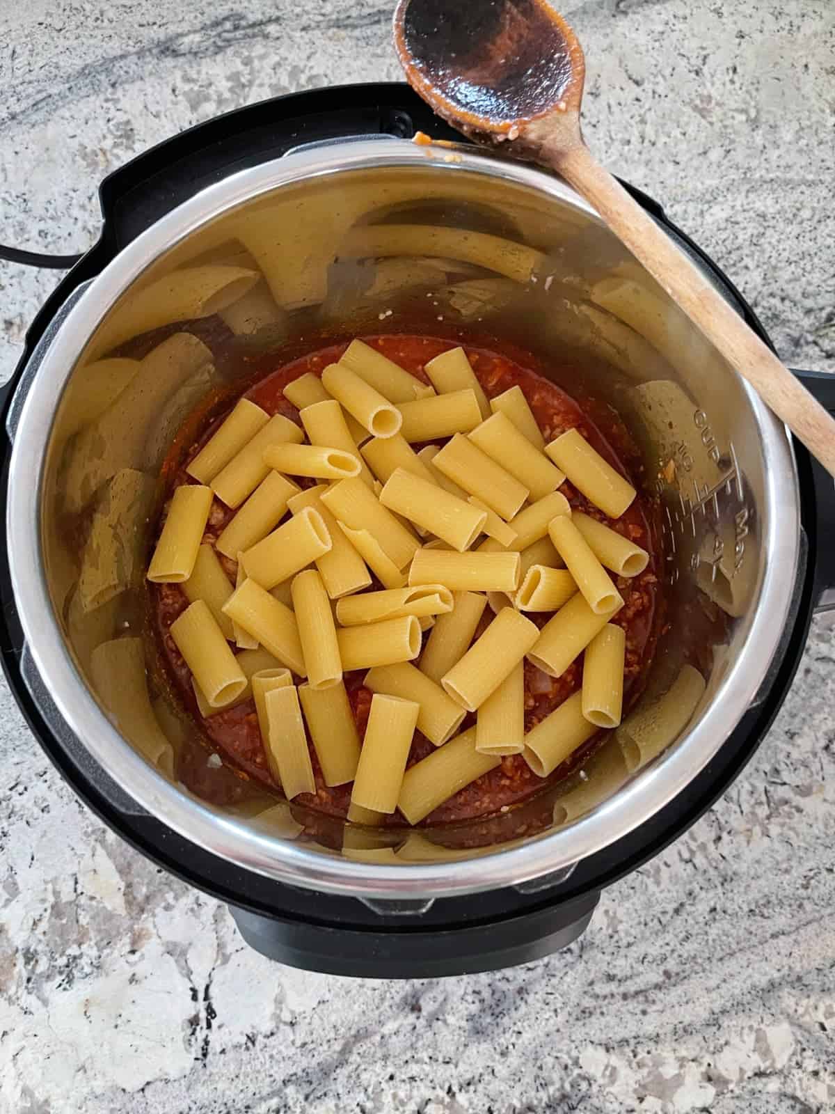 Adding uncooked rigatoni to meat sauce in instant pot.