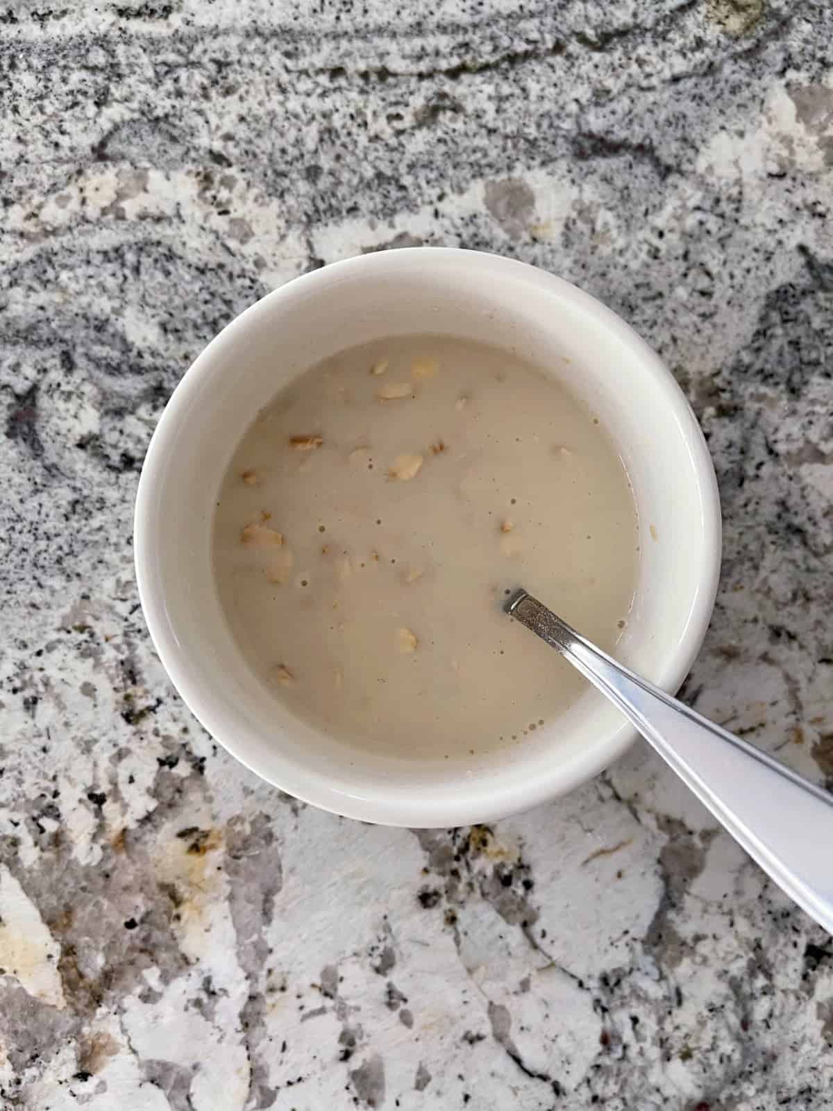 Stirring oats, almond milk and cheesecake Jello instant pudding mix in small white bowl with spoon.