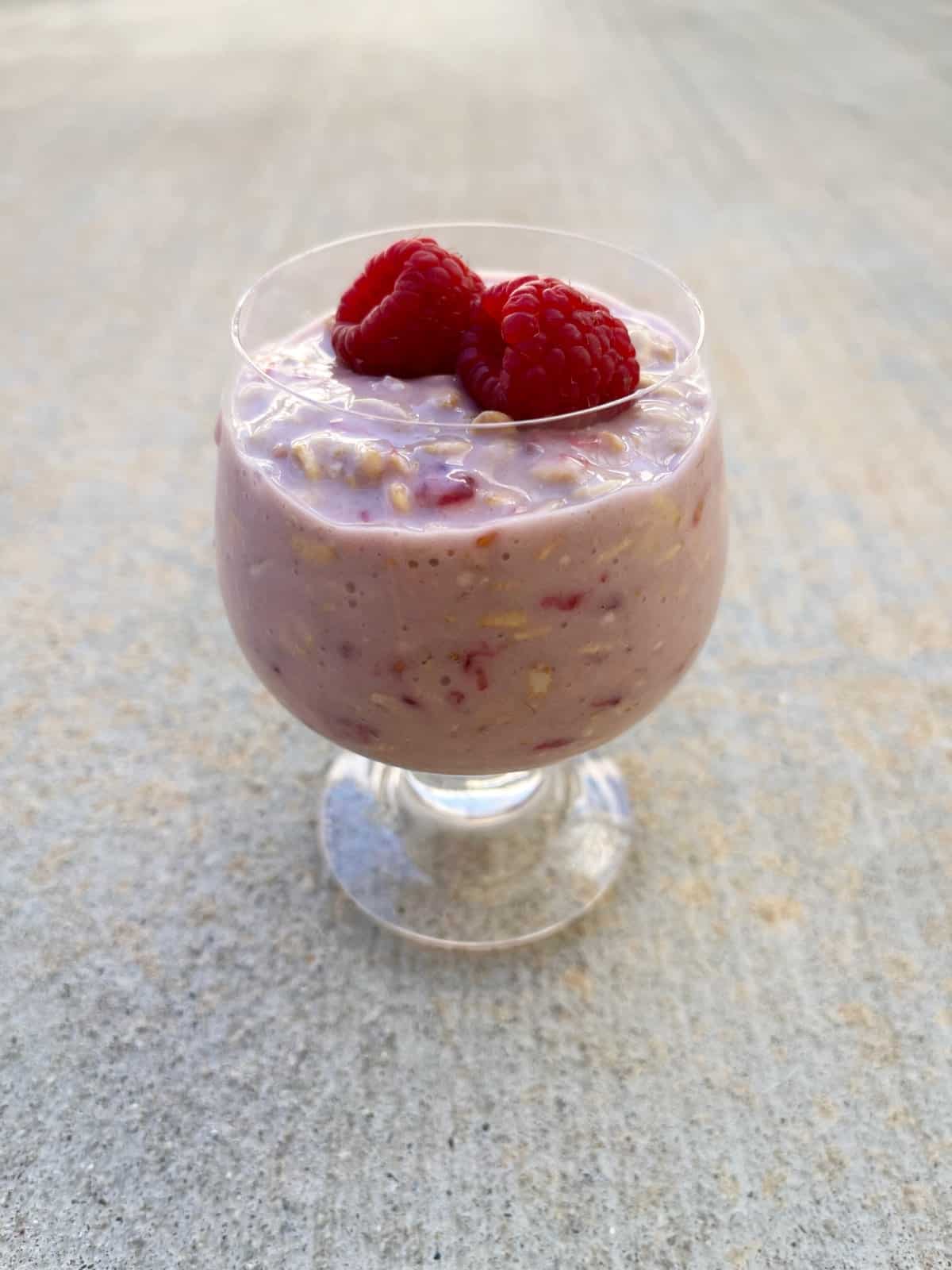 Very raspberry cheesecake overnight oats in stemmed glass.
