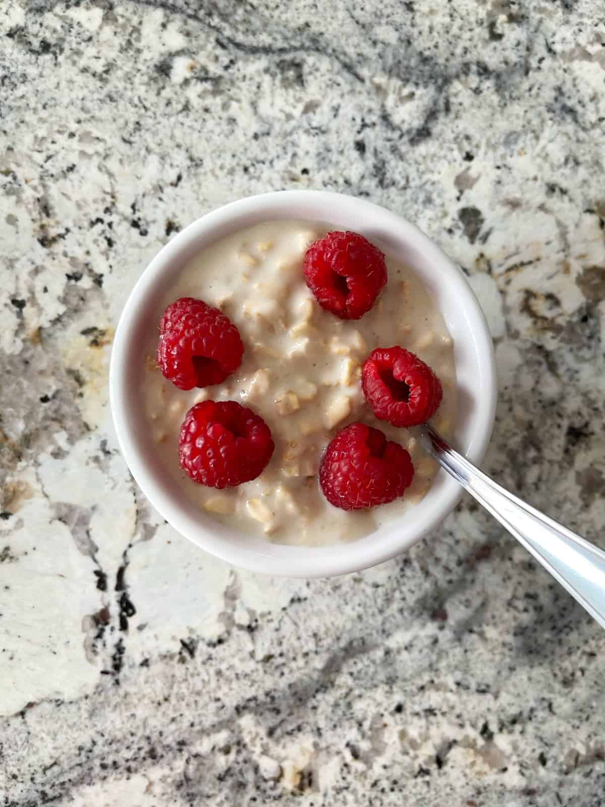 Raspberry cheesecake overnight oats in white bowl with spoon.
