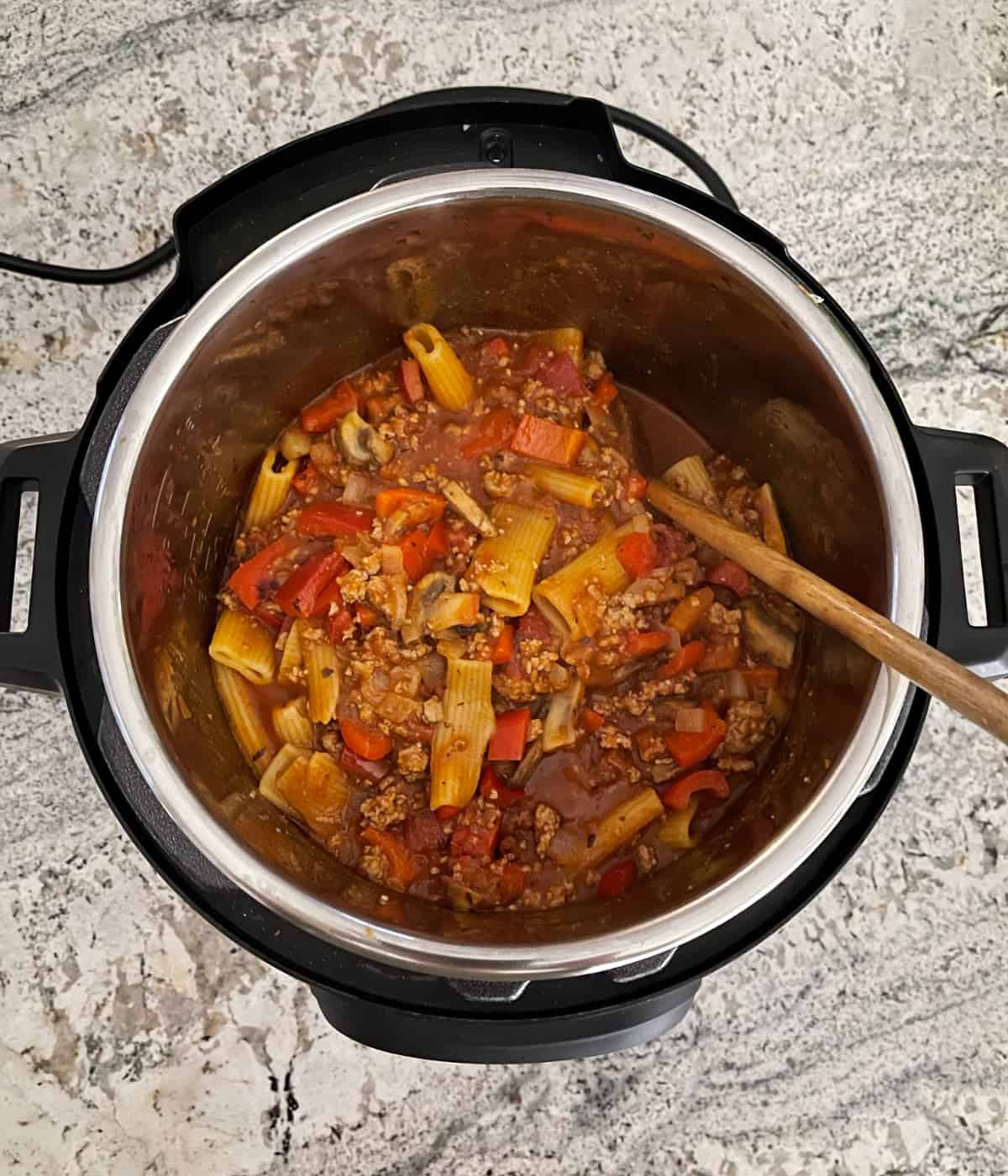 Stirring rigatoni and meat sauce in instant pot with wooden spoon.