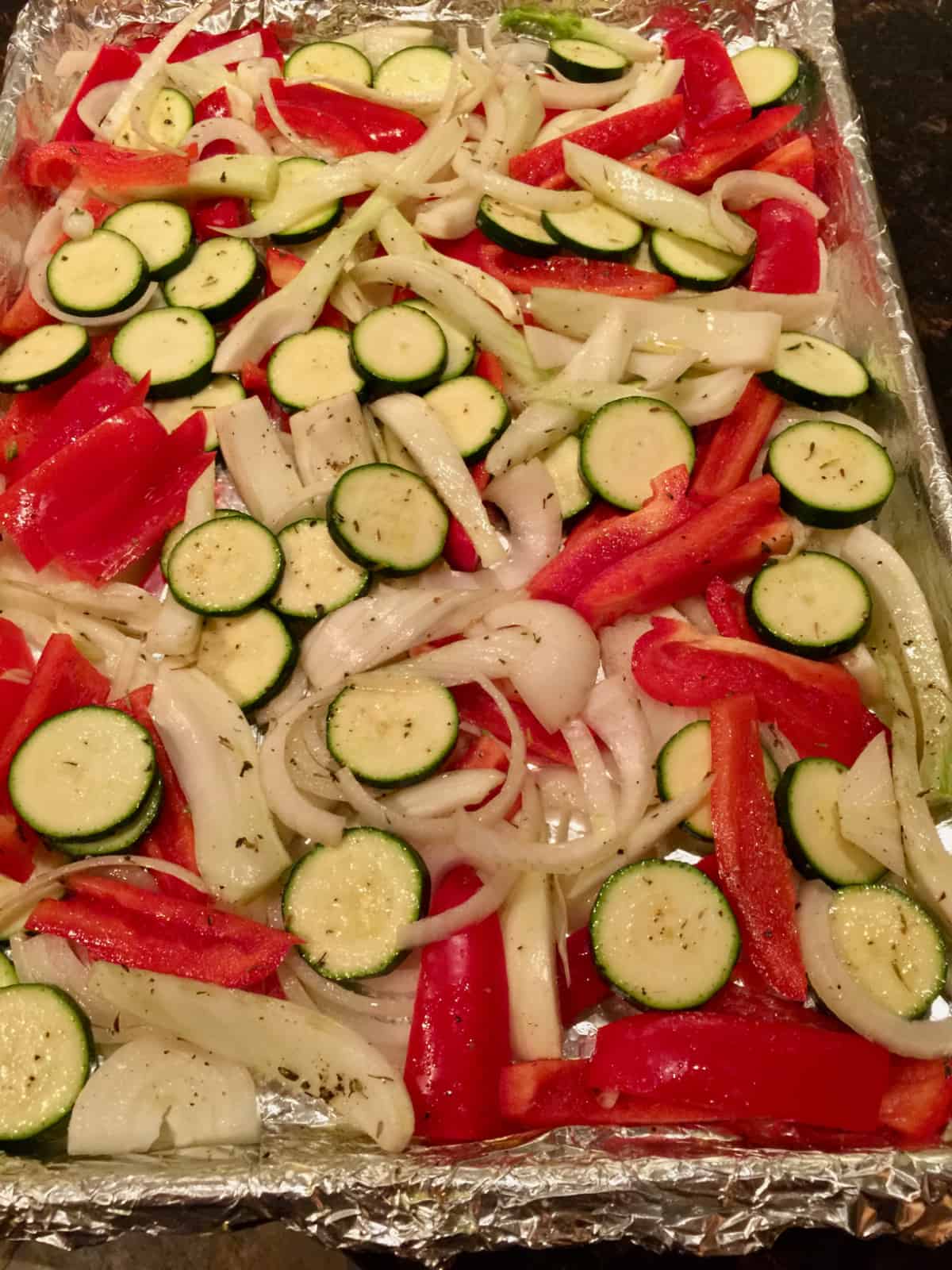 Foil-lined sheet pan with zucchini, onions and peppers.