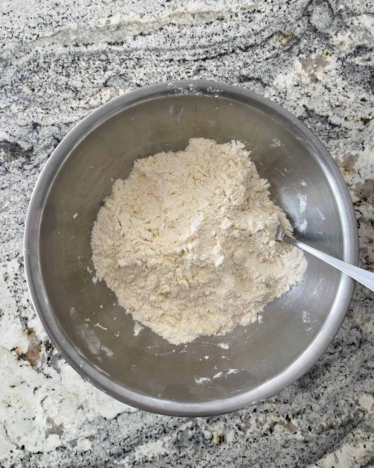 Cutting cold butter into all-purpose flour mixture with fork in mixing bowl.