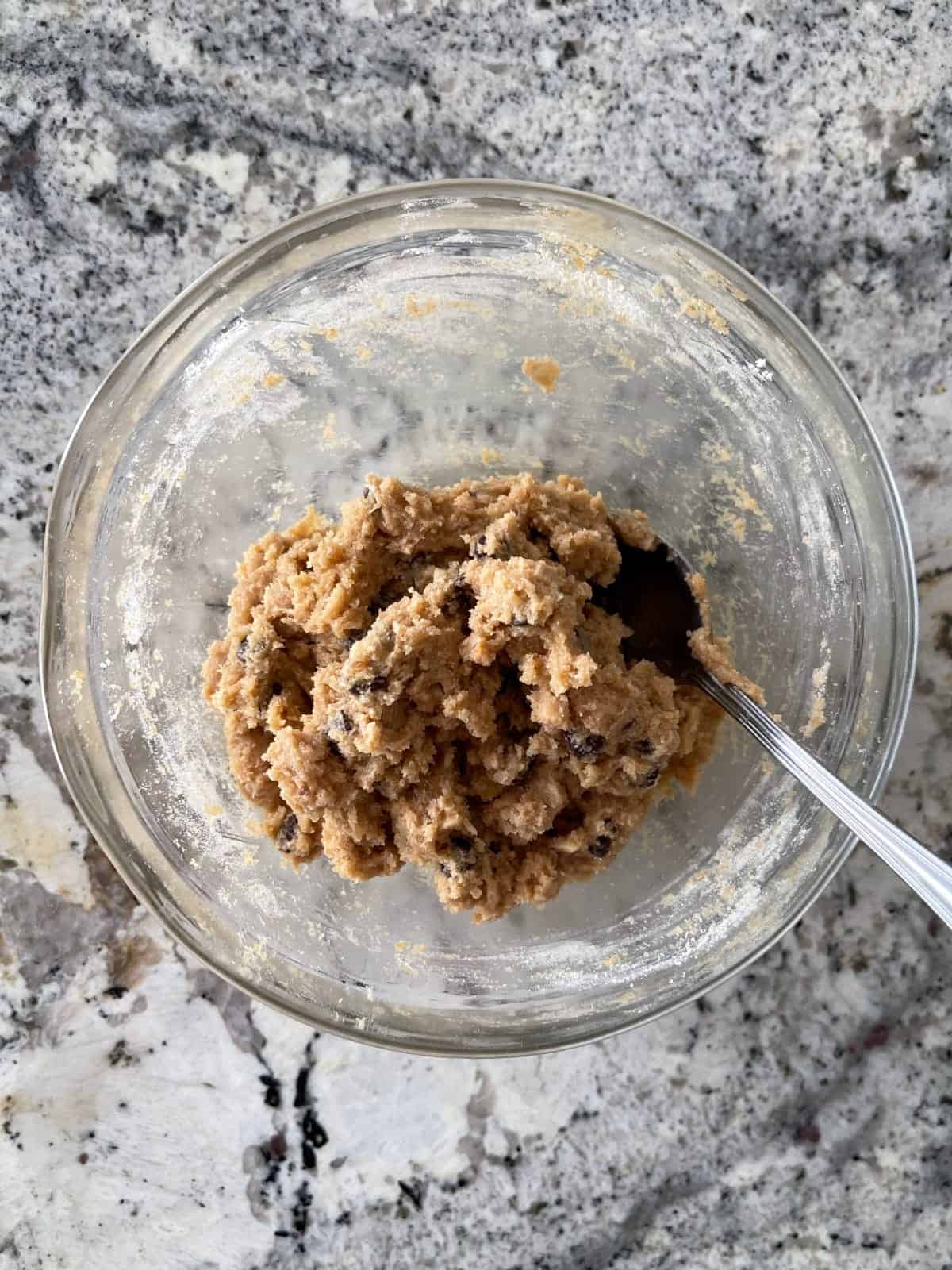 Mixing chocolate chip cookie dough batter in small glass bowl with spoon.