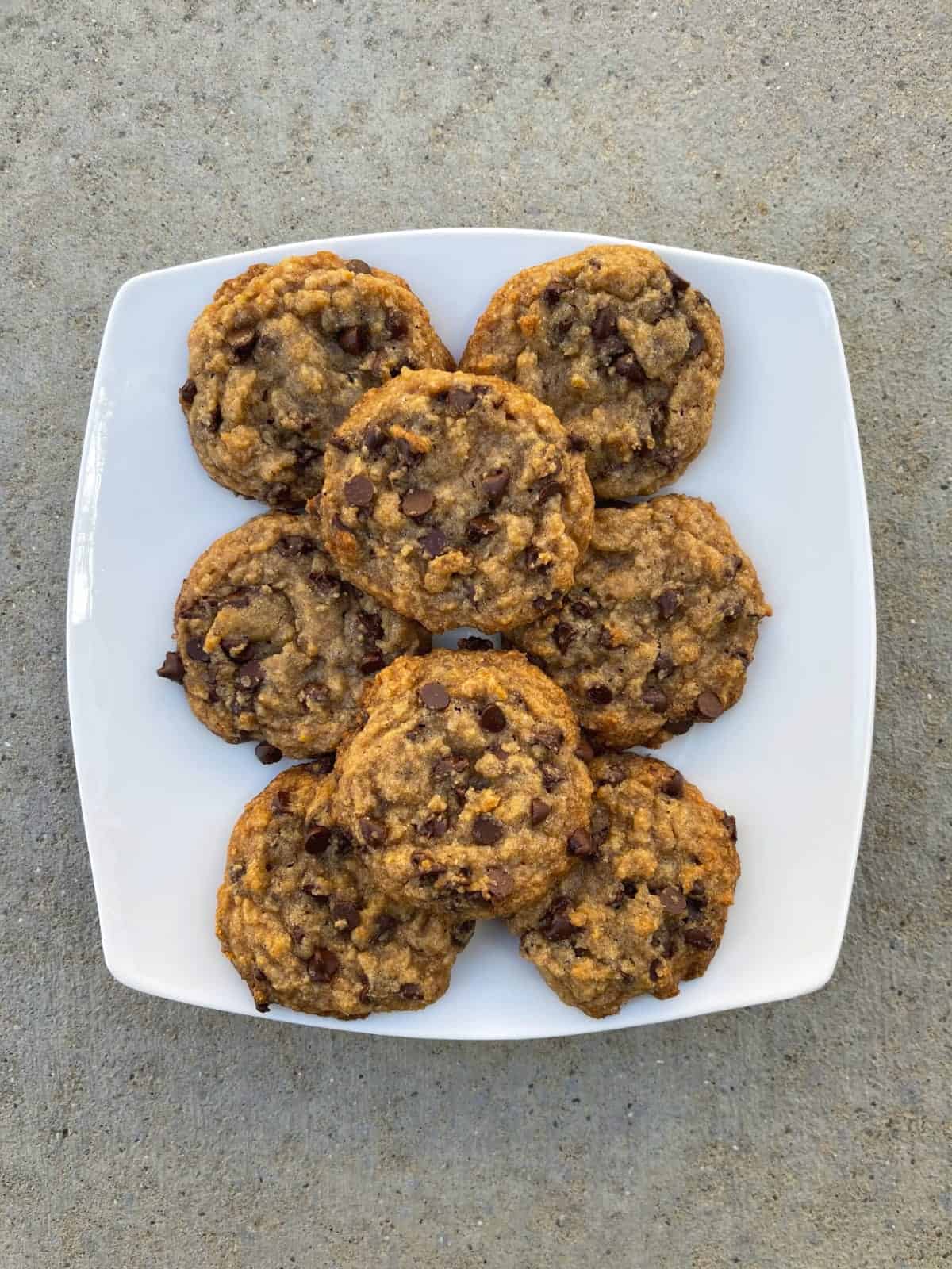 Tablespoon chocolate chip cookies stacked on white plate.