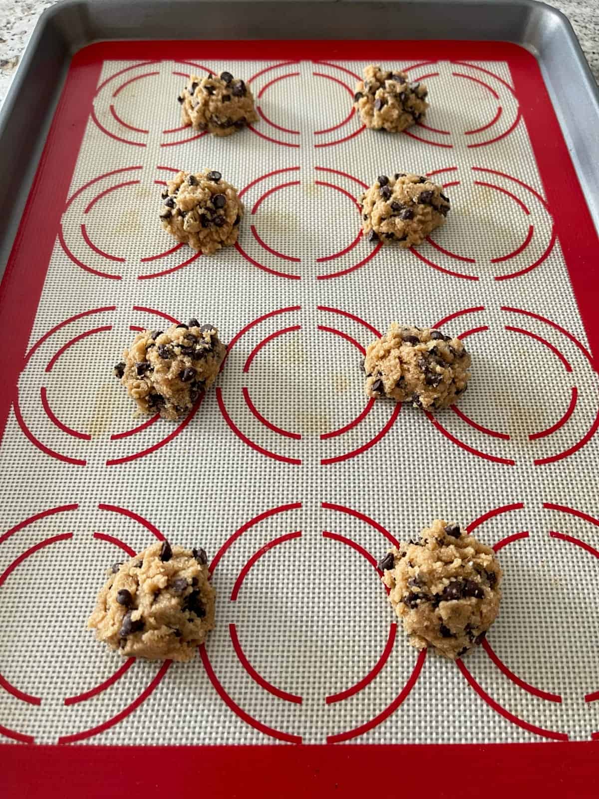 Unbaked tablespoon chocolate chip cookies on silpat lined baking pan.