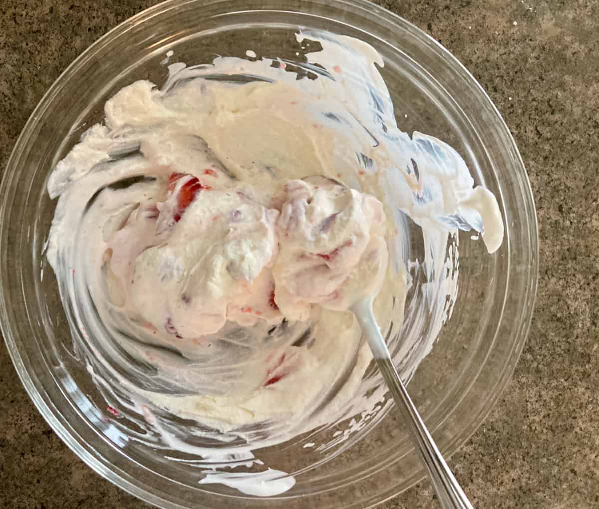Mixing strawberries, yogurt and lite whipped topping in glass bowl with spoon.