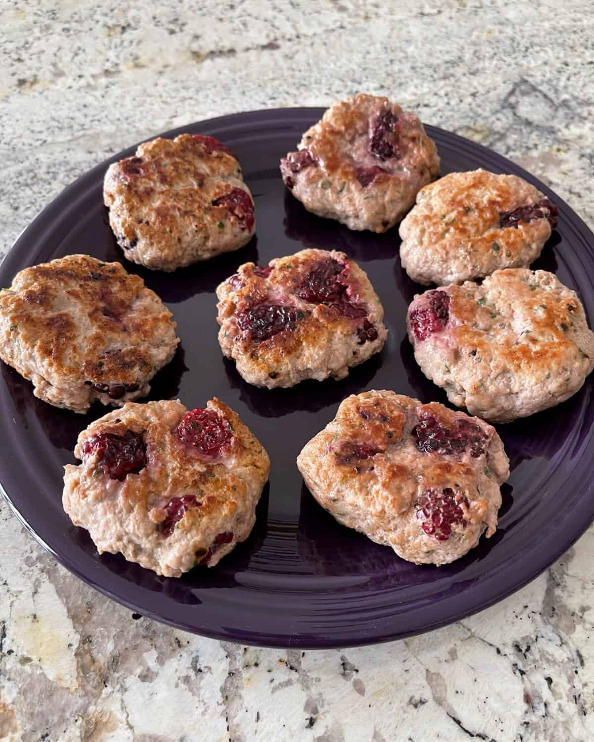 Fresh blackberry breakfast sausage patties with thyme and sage on purple serving platter.
