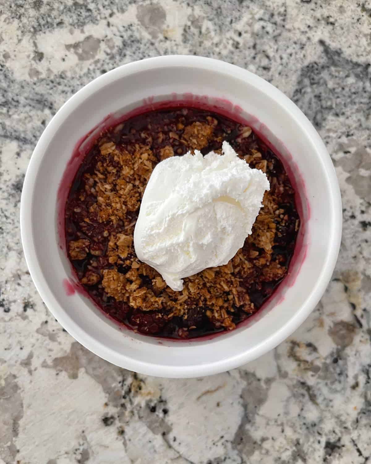 Easy blackberry crisp topped with lite whipped cream in white ramekin.