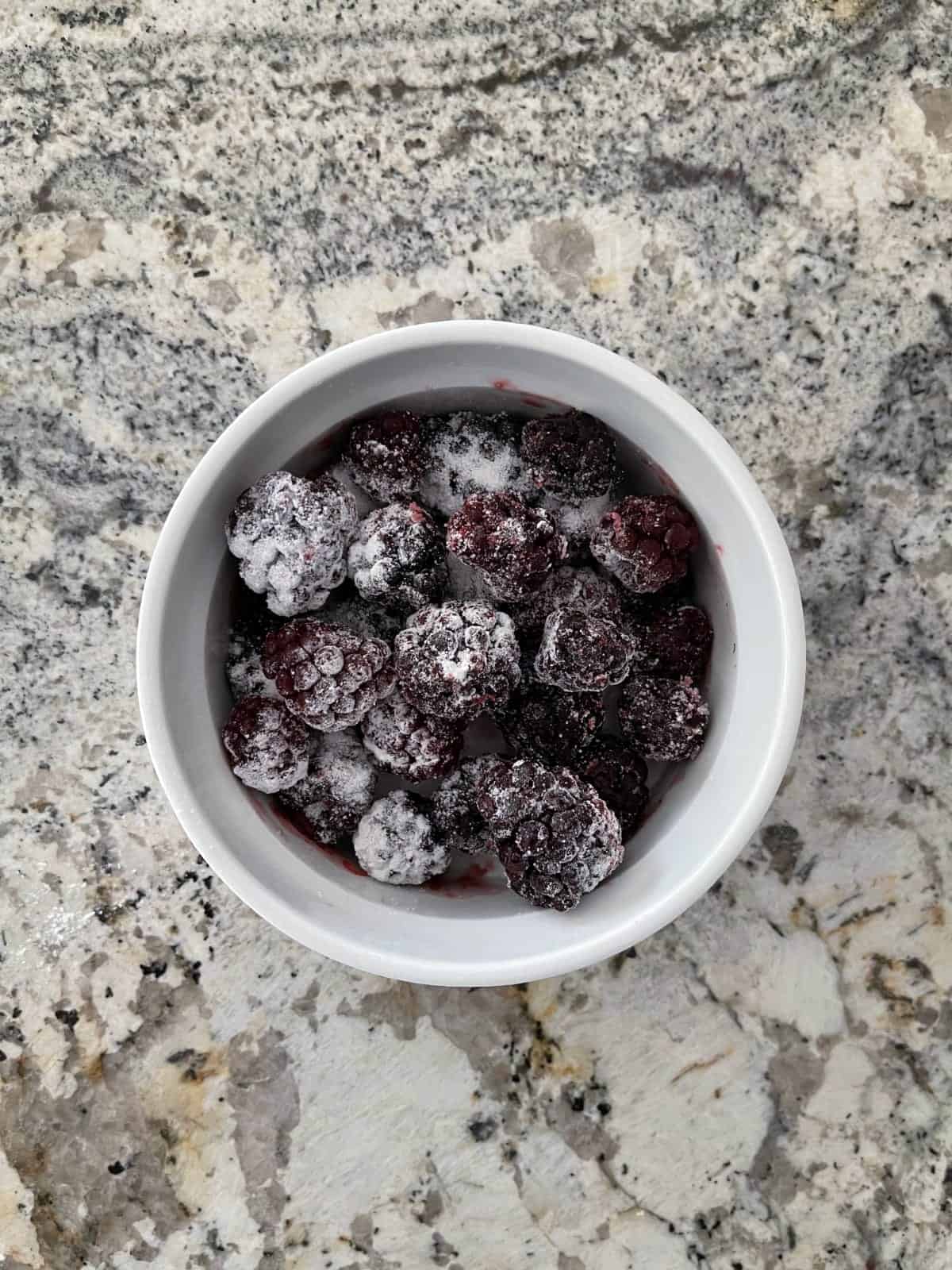 Frozen blackberries stirred with zero calorie sweetener in white ramekin.
