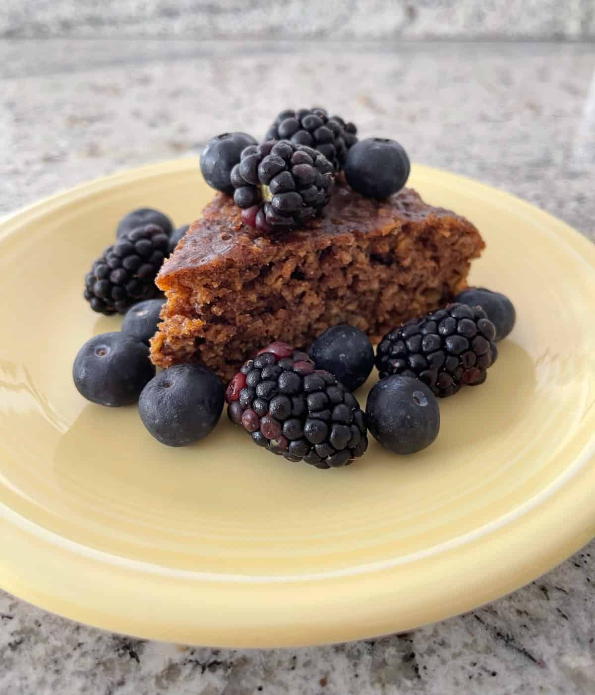 Piece of flourless banana oat cake topped with blueberries and blackberries on yellow plate.